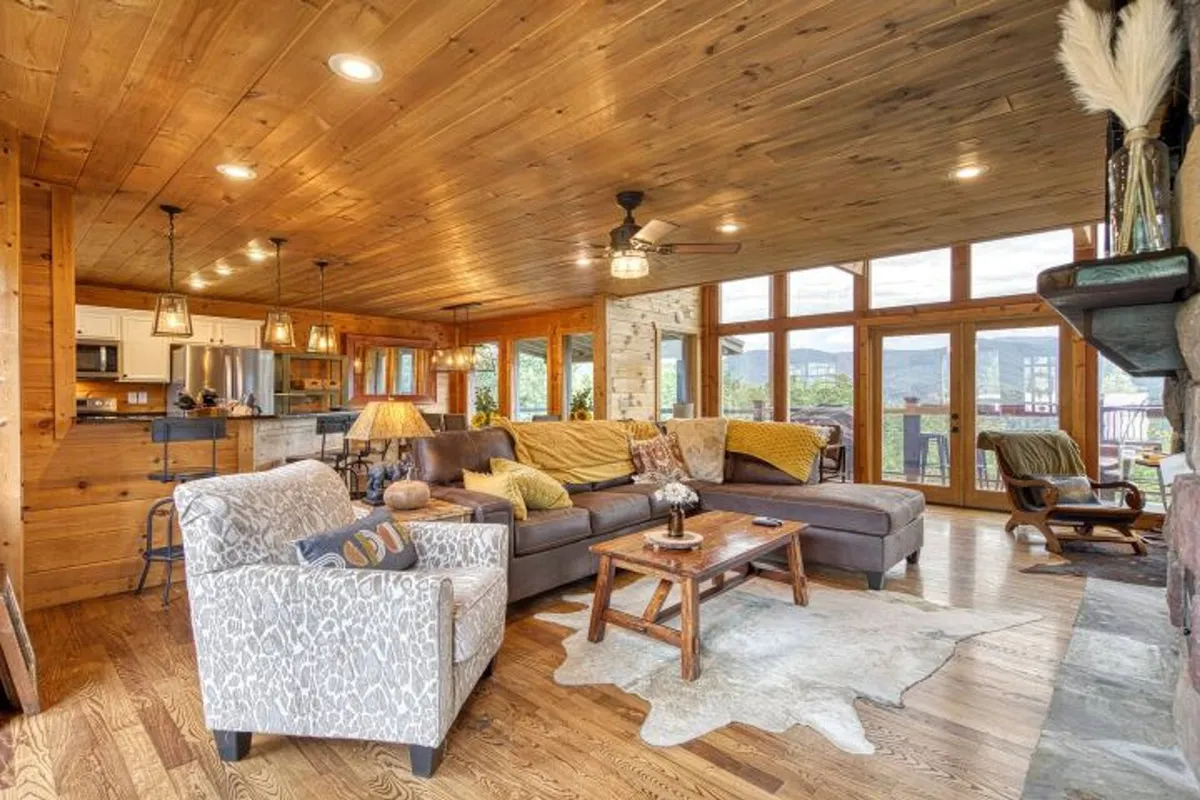 A cozy living space with expansive windows framing the sunrise over the Smoky Mountains. The inviting sectional sofa offers a perfect vantage point for enjoying morning coffee, reading, or gathering with loved ones while staying connected to the outdoors through panoramic views.