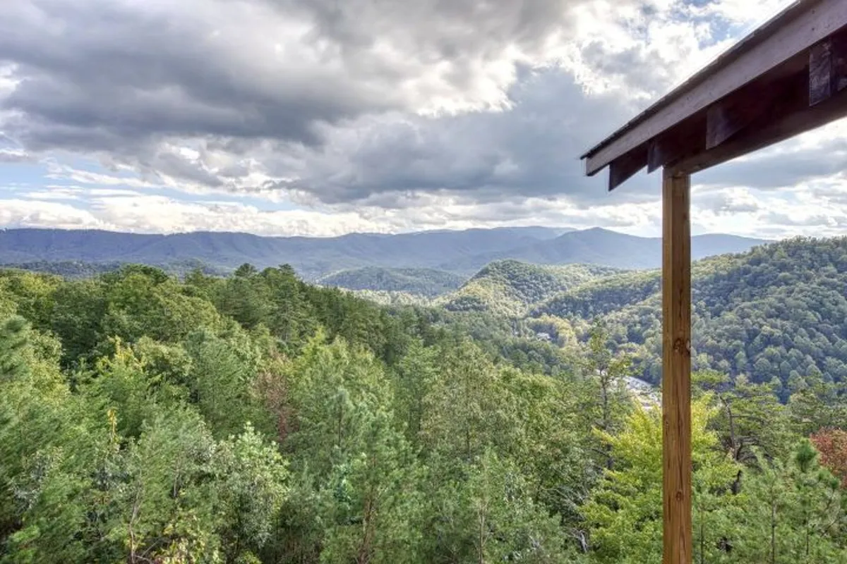 A panoramic view of expansive mountain ranges and dense forest, with a wooden structure in the foreground. The scene evokes a sense of adventure, perfect for guests looking to explore or capture group moments in nature.