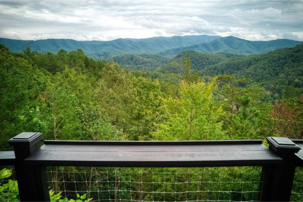 A breathtaking vista of a mountain range unfolds beyond a wooden railing, with lush greenery in the foreground. The wide, open view is tranquil and awe-inspiring, perfect for watching sunsets or stargazing. The scene encapsulates the panoramic beauty described in the section.