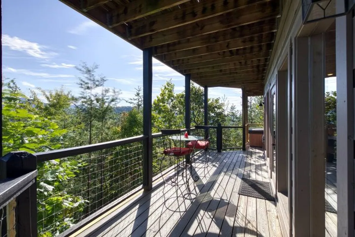A serene wooden deck with a cozy red chair, looking out over scenic mountain views. The deck is bathed in gentle natural light, perfect for enjoying morning coffee or relaxing under the stars. The privacy and tranquility of the space are emphasized by the surrounding trees.