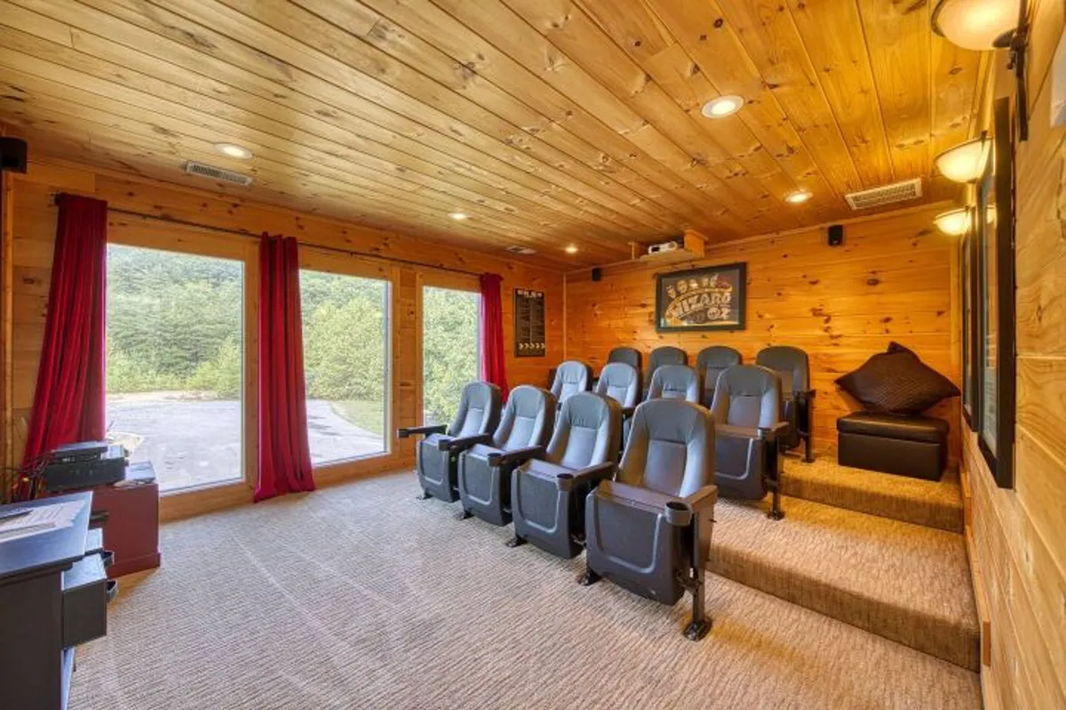 Another angle on a home theater space, this image features comfortable theater seating, large windows with natural light, warm wooden paneling, and dramatic red curtains framing the room. The setting is both luxurious and relaxed, emphasizing group enjoyment.