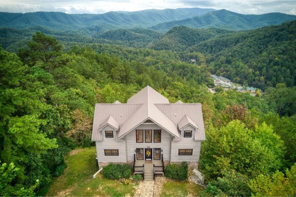A wide exterior view of the estate nestled among scenic mountains and a lush tree line. The house is inviting, with a peaceful porch area perfect for relaxing or congregating before venturing out to explore local attractions.